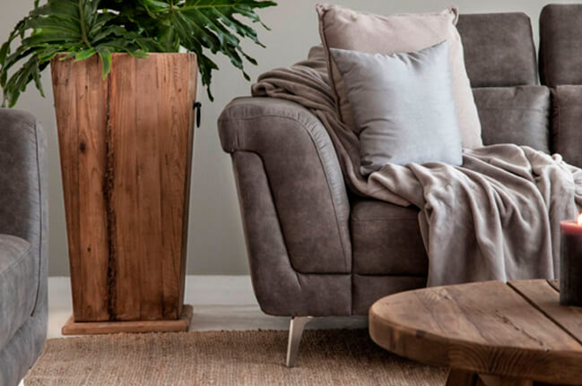 Close up view of grey couch styled with grey scatter cushions next to a wooden planter with green plant in